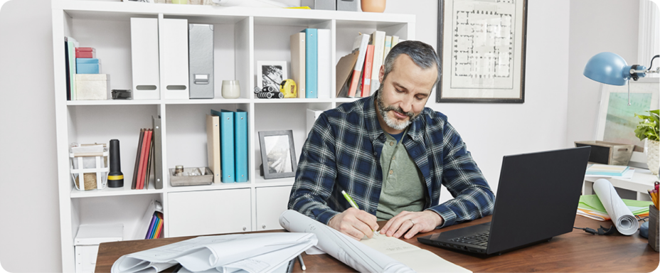 Bearded man seated by a desk and writing on paper